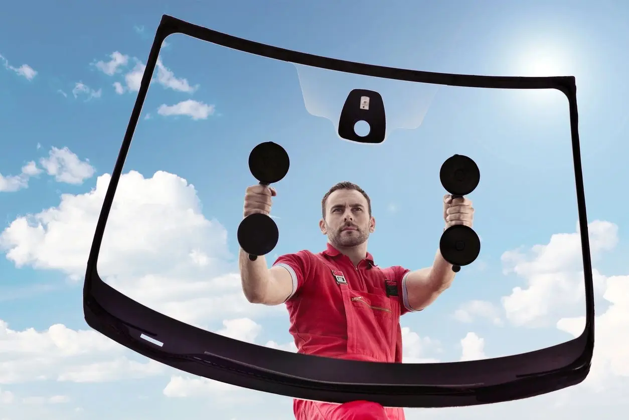 A man is holding two black dumbbells in front of a car window.